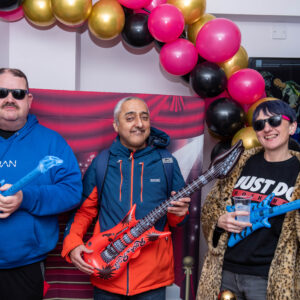 2 men and a woman posing with inflateable guitairs under a baloon arch