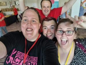 A young woman in a Gig Buddies t-shirt taking a selfie with her 3 friends